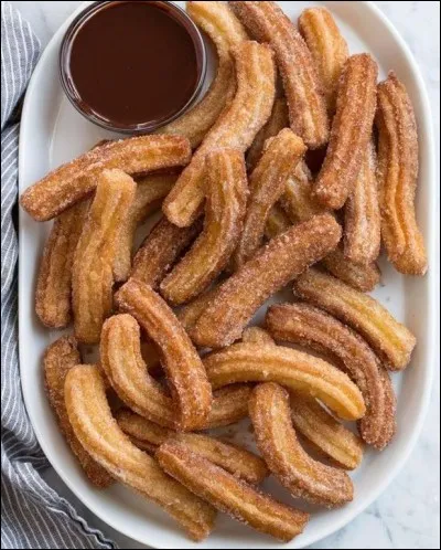 Churros : pâtisserie en pâte frite. Présentée sous la forme d'un gros spaghetti ou d'un beignet. 
Patatas bravas : pommes de terre coupées en cubes irréguliers et frites dans de l'huile d'olive avec quelques gousses d'ail.
Quel est le pays d'origine de ces deux plats ?